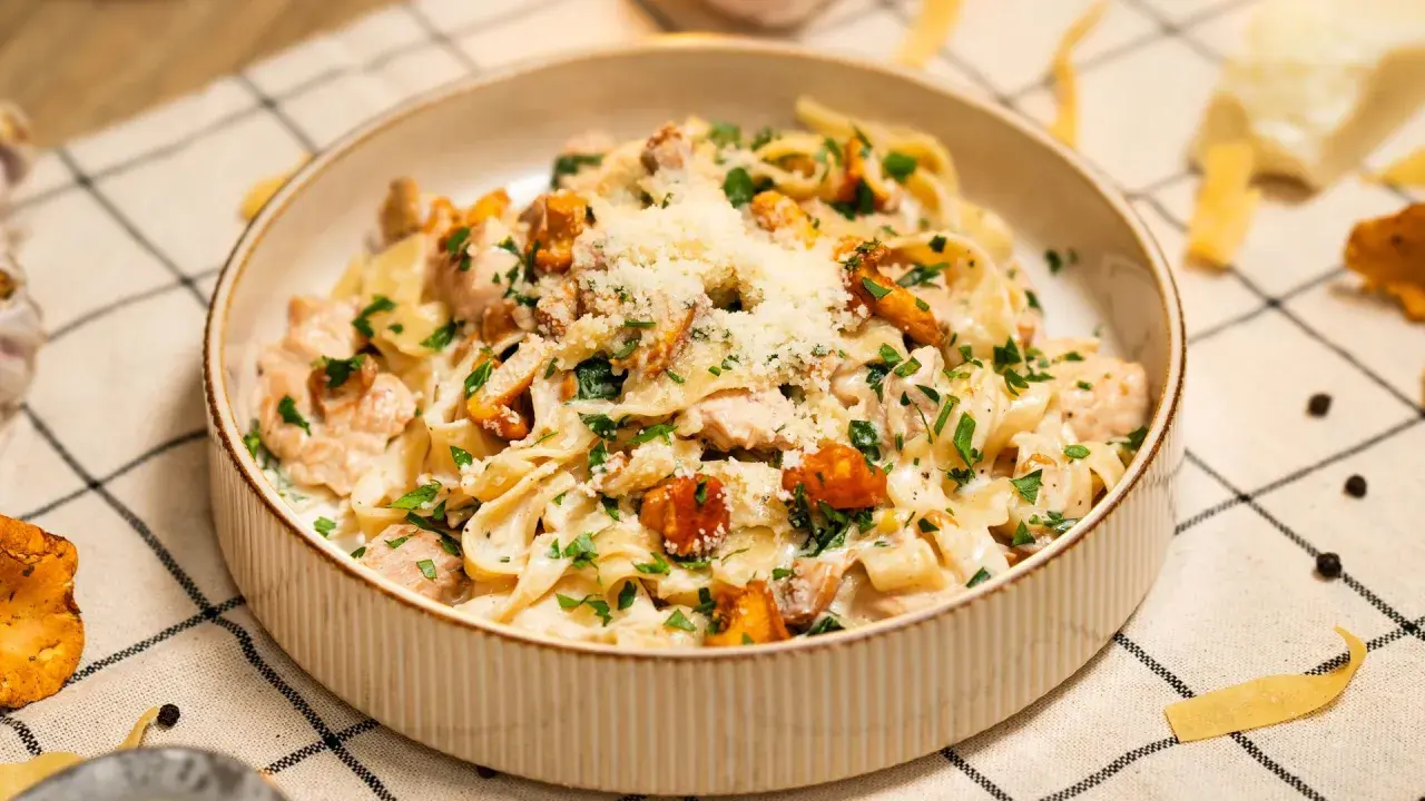 Pyszny makaron w sosie kurkowym z kawałkami kurczaka i posypany parmezanem.