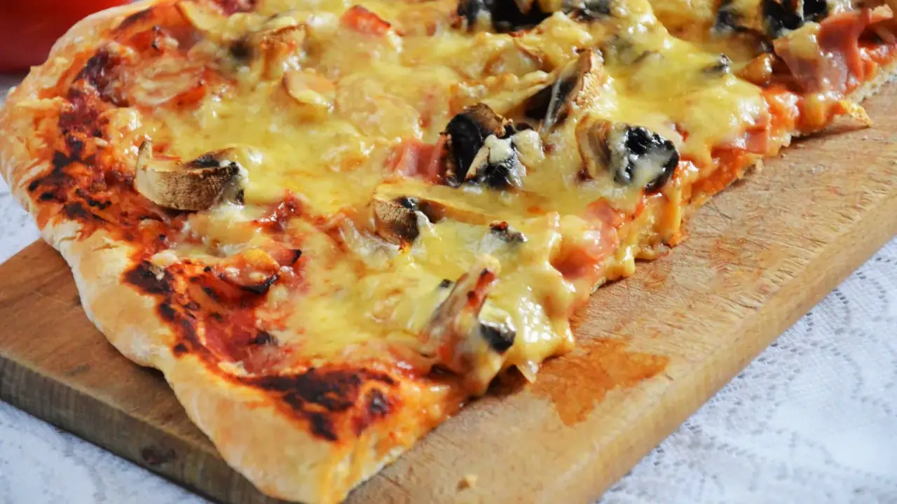 Pyszna pizza capriciosa z pieczarkami i szynką, roztopiony ser ciągnie się na chrupiącym cieście.