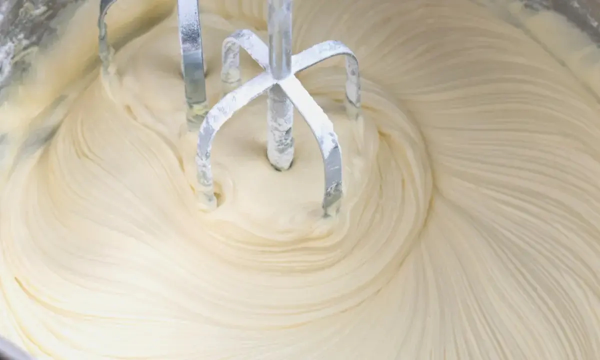 Mieszadła miksera zagłębiają się w puszysty krem z mascarpone i białej czekolady, tworząc faliste wzory.