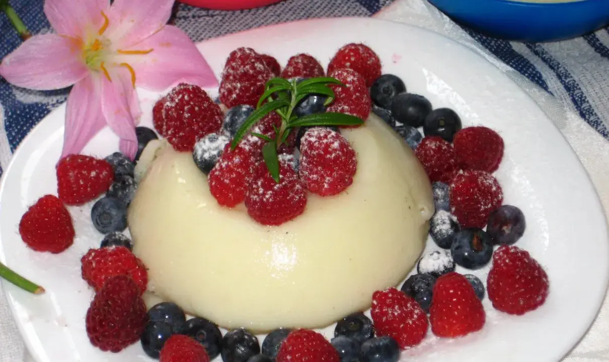Panna cotta z malinami i borówkami, posypana cukrem pudrem. Idealny deser, który można zrobić według prostego legumina przepisu.