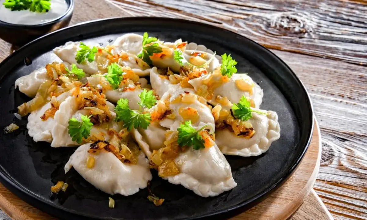 Pyszne pierogi ukraińskie, polane skwarkami i posypane natką pietruszki, podane z miseczką śmietany.