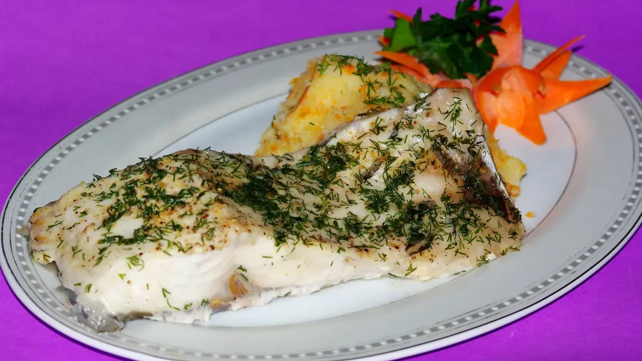 Pieczony amur z koperkiem i puree ziemniaczanym, ozdobiony marchewką i natką pietruszki.