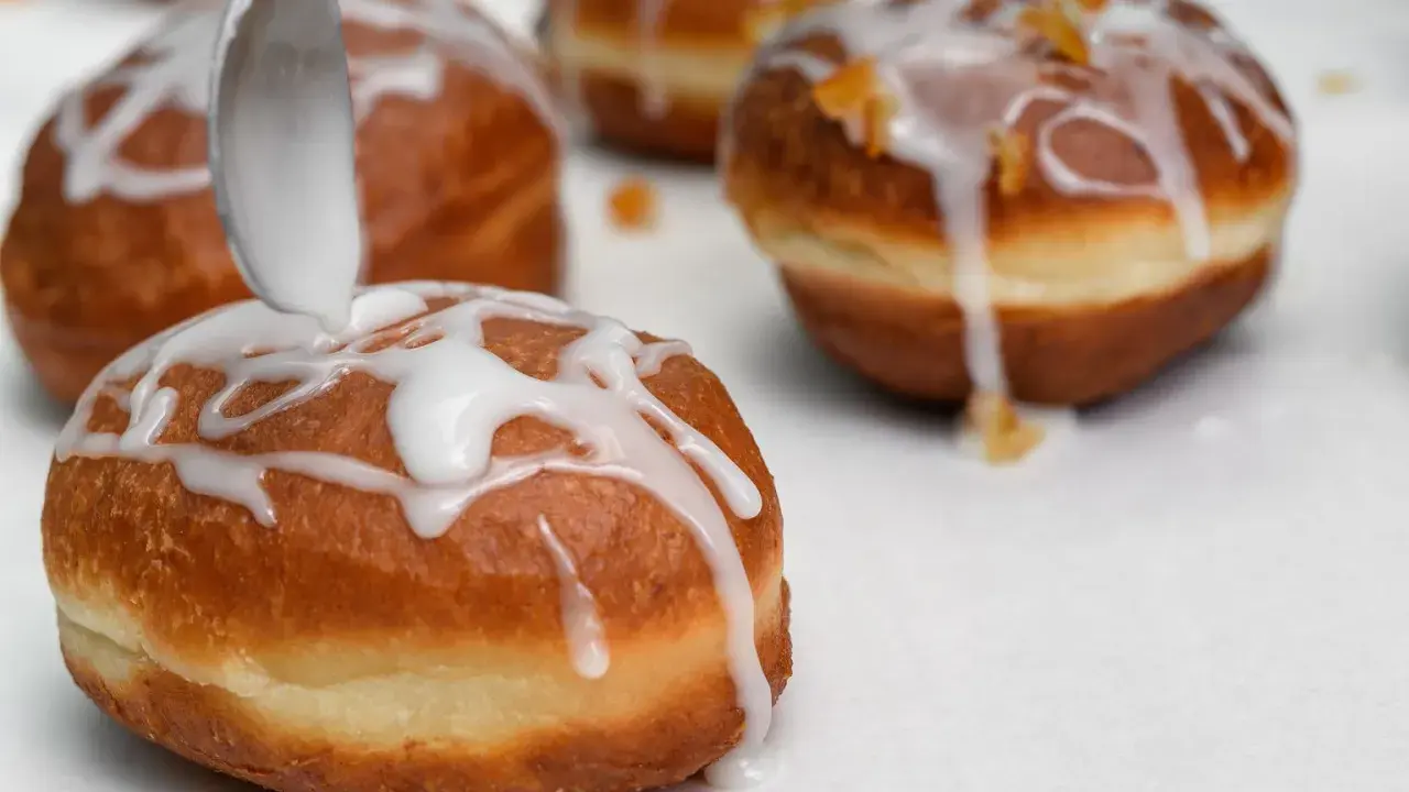 Lukier przepis na pączki. Łyżka polewa słodką masą pączki, które zaraz trafią na stół.