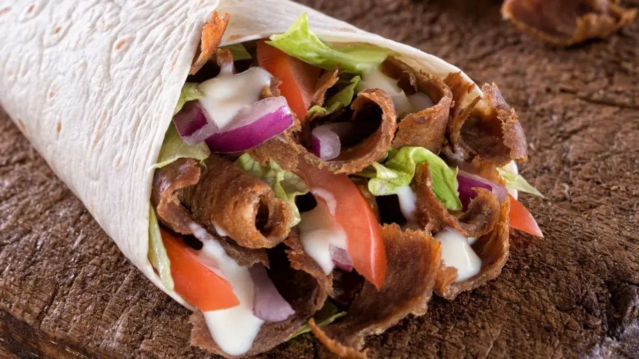 Pyszny, domowy kebab zawinięty w tortillę z soczystym mięsem, chrupiącą sałatą, pomidorami i cebulą, polany sosem.