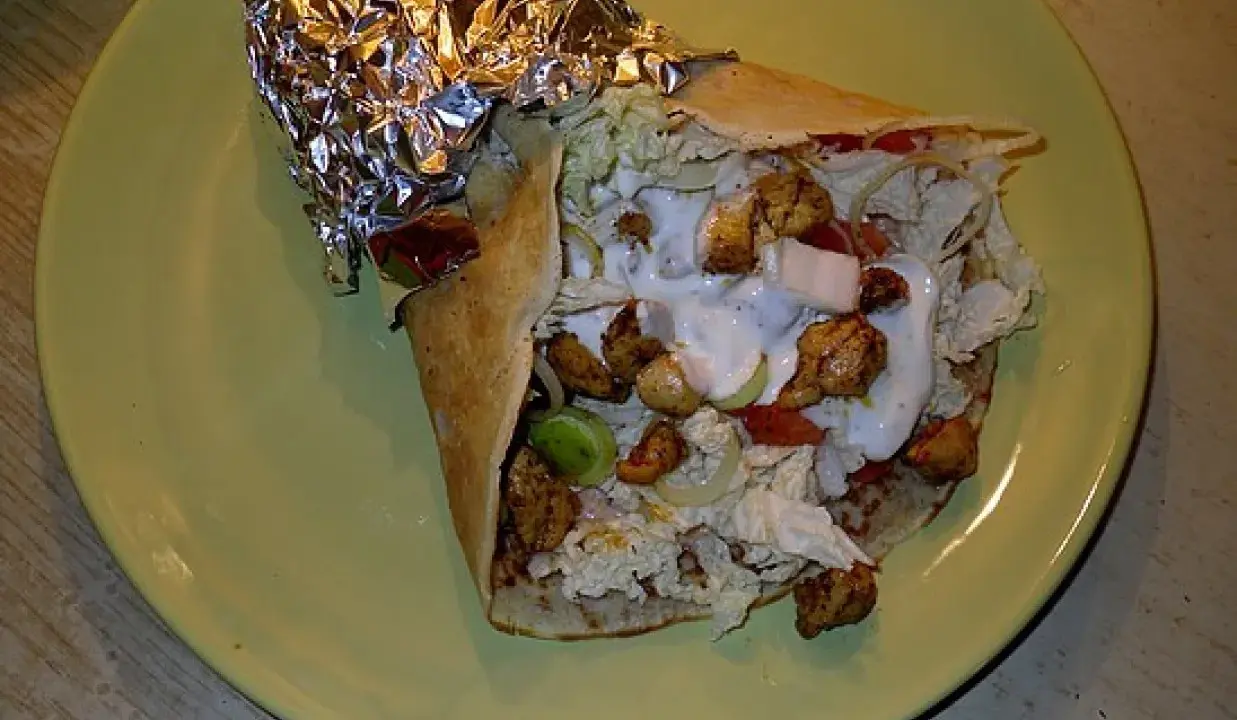 Pyszny kebab w tortilli z kurczakiem, warzywami i sosem na zielonym talerzu.