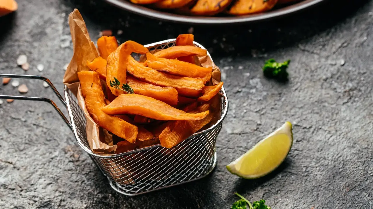 Chrupiące frytki z batatów z frytkownicy airfryer, podane w metalowym koszyku, z limonką i natką pietruszki.