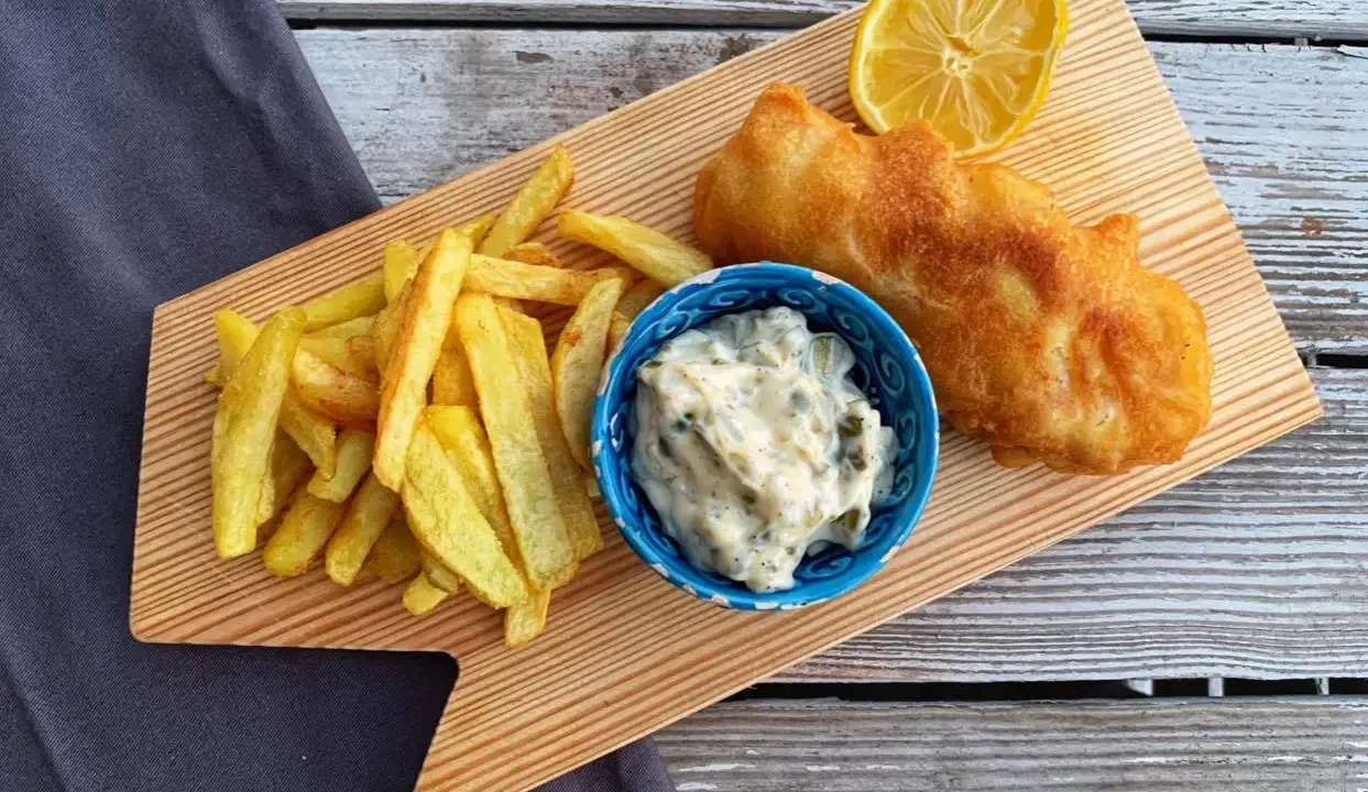 Chrupiące fish and chips z cytryną i sosem tatarskim na drewnianej desce.