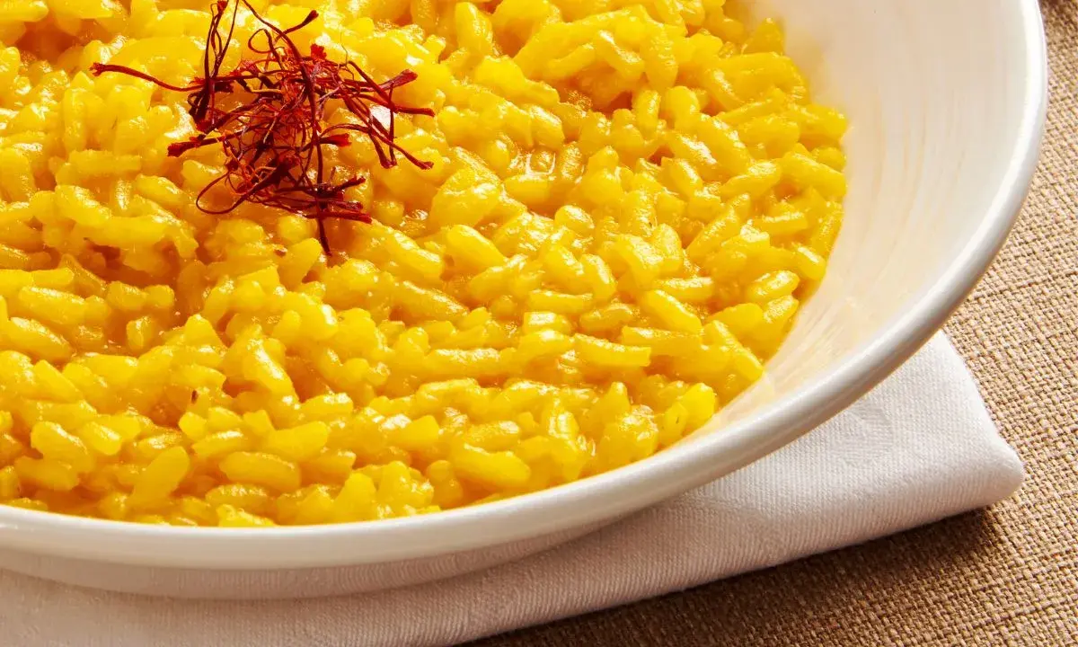 Aksamitne risotto alla milanese, złociste od szafranu, podane w białej misce, ozdobione nitkami szafranu.