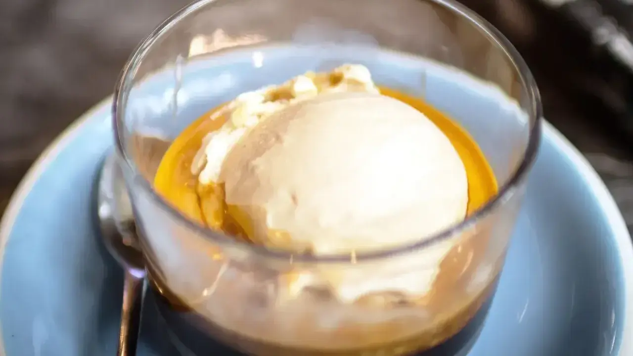 Pyszne affogato: gałka lodów waniliowych w gorącym espresso, podana w szklance na niebieskim talerzyku.