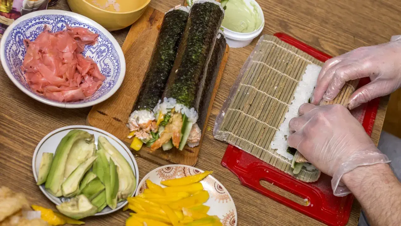 Przygotowanie uramaki: ryż, awokado, mango, krewetki i marynowany imbir czekają na zwinięcie w pyszne rolki sushi.