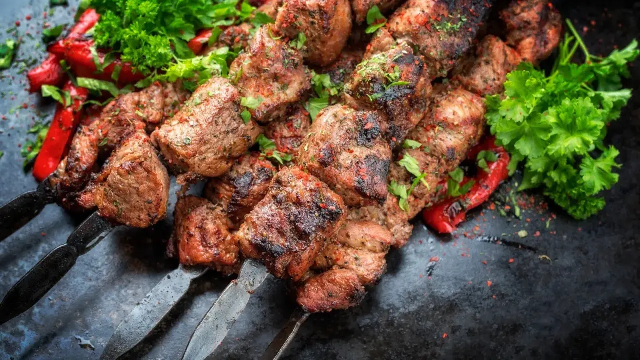 Soczyste kawałki mięsa na szpadach, przypominające kofta kebab, podane z pieczoną papryką i świeżą natką pietruszki.