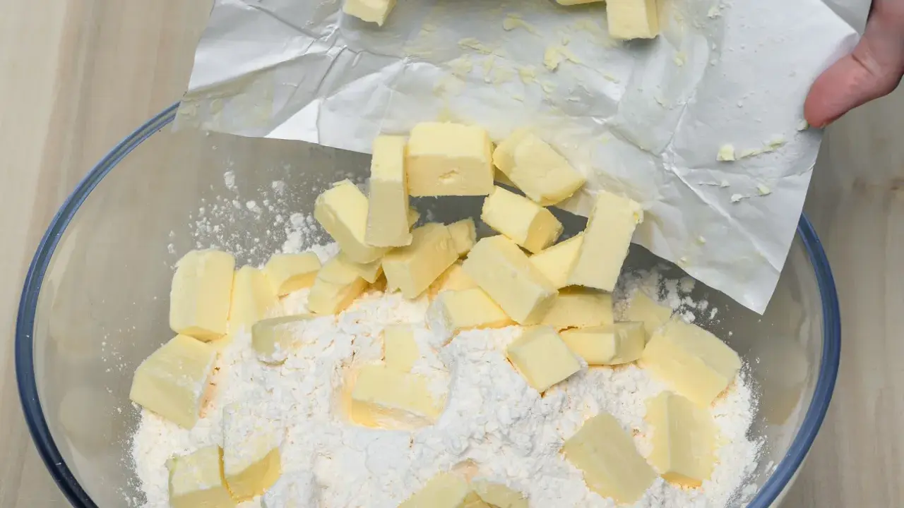 Kawałki zimnego masła dodawane do mąki w misce, kluczowy krok w sprawdzonym przepisie na kruche ciasto.