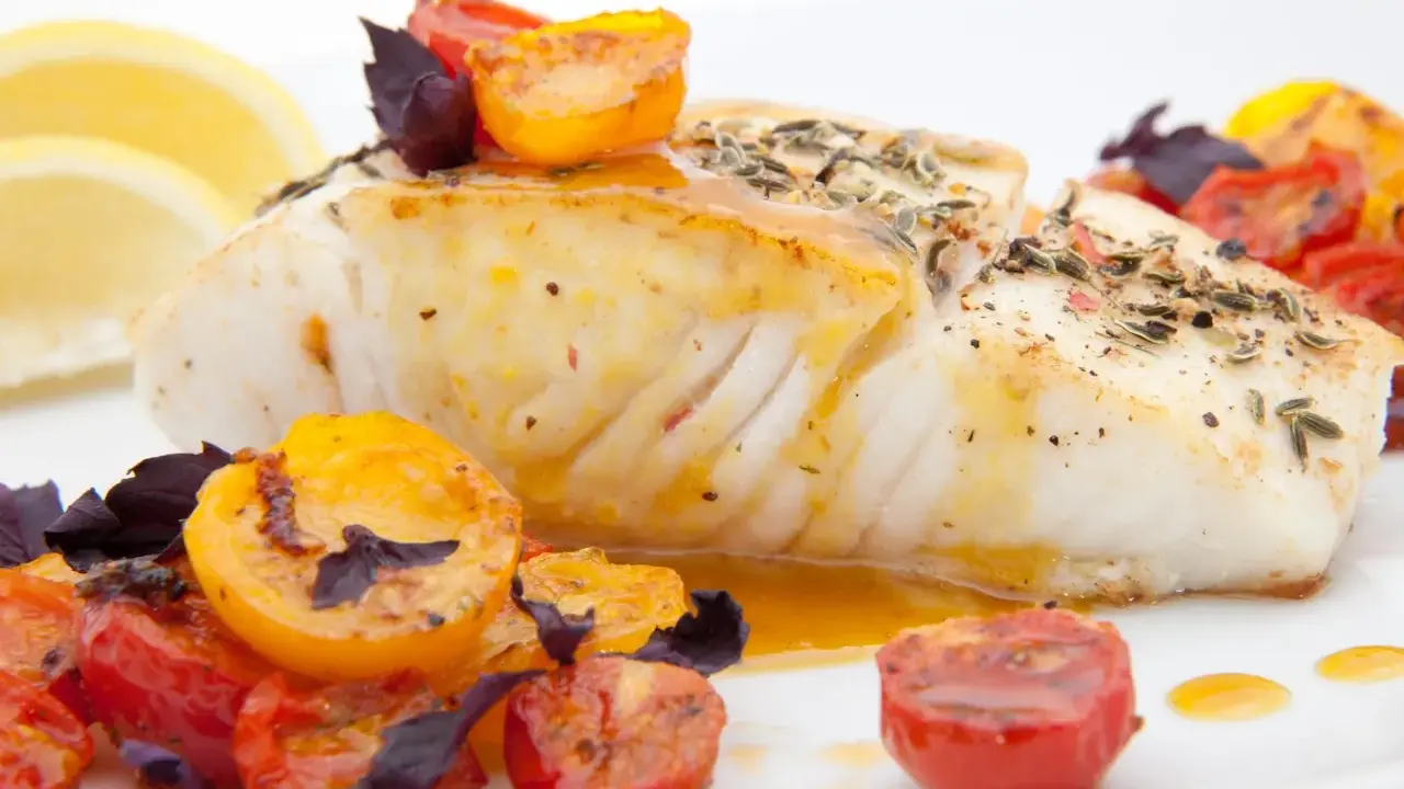Pyszny halibut ryba, pieczony z pomidorkami koktajlowymi i ziołami, podany z cytryną.