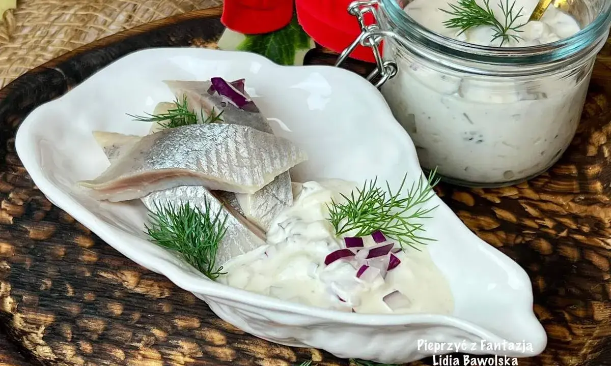 Matiasy w śmietanie z cebulą i ogórkiem, udekorowane koperkiem, prezentują się apetycznie.