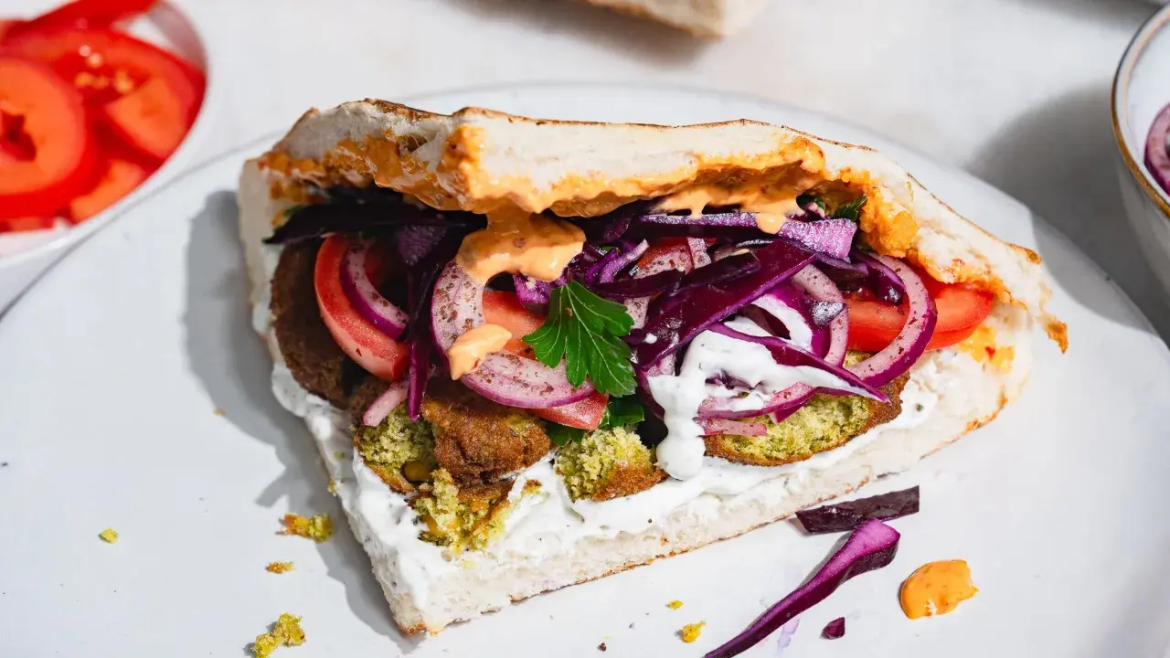 Pyszny falafel kebab w bułce z pomidorami, czerwoną cebulą, kapustą i sosami.