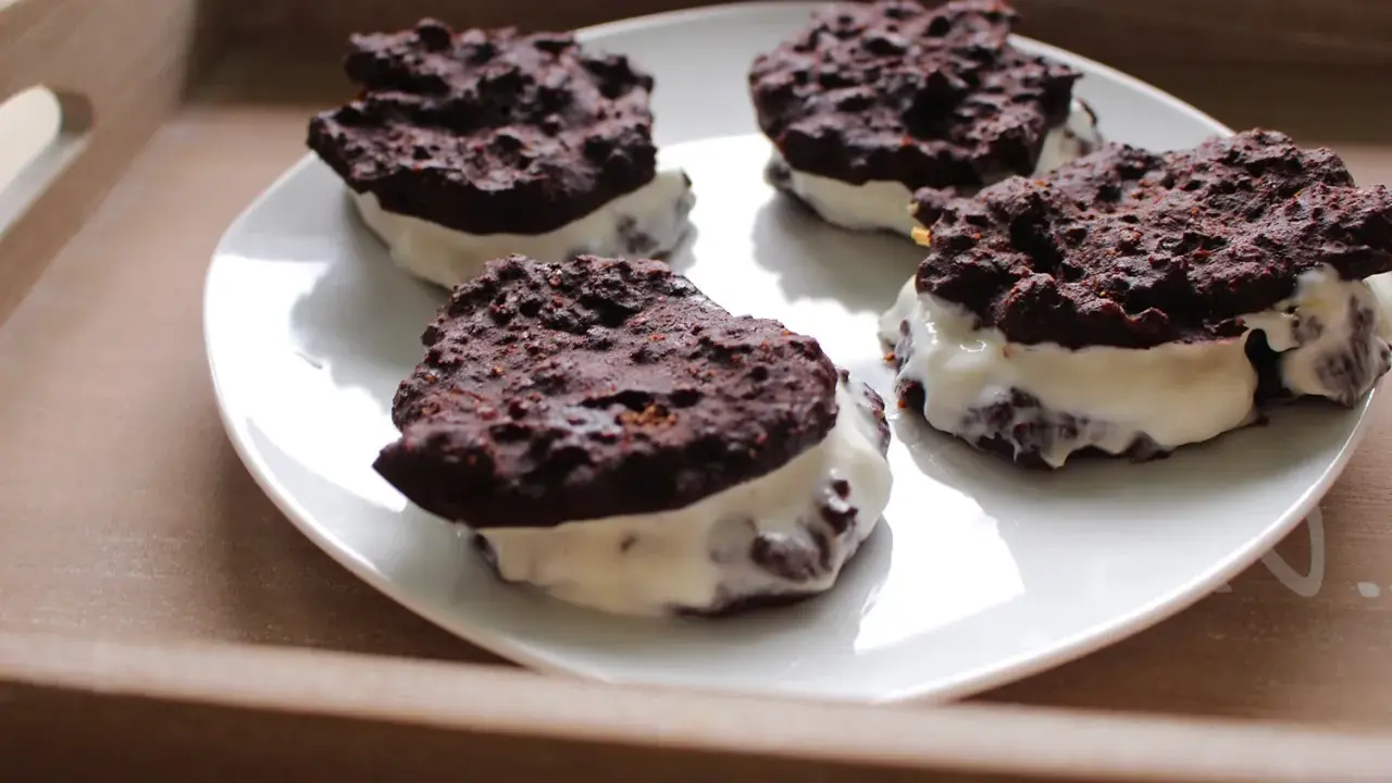 Cztery domowe ciastka Oreo z kremowym nadzieniem, ułożone na białym talerzu.