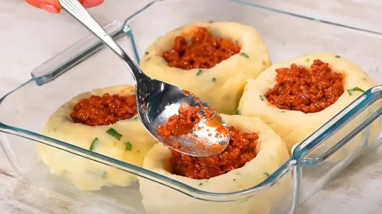 Łyżka nakłada mięsne nadzienie do wgłębień w ziemniaczanych grule, przygotowywanych w szklanym naczyniu.