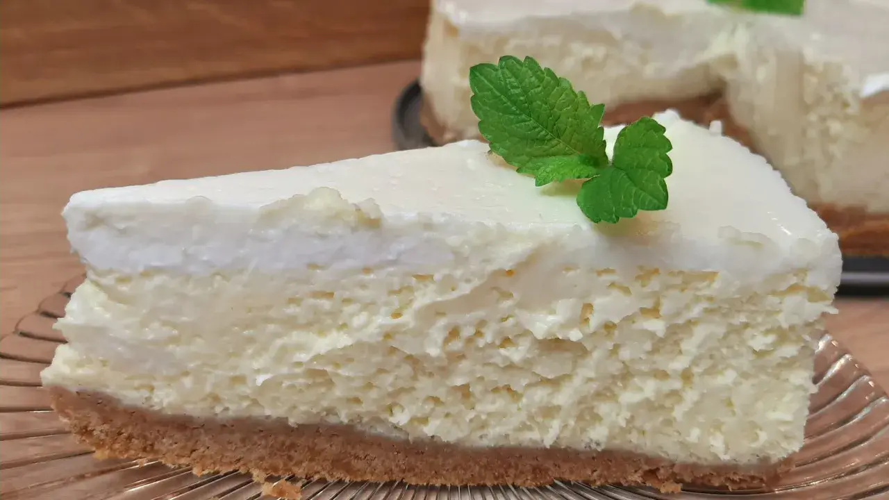 Pyszny sernik ze śmietaną kremówką, udekorowany listkiem mięty, na kruchym spodzie.