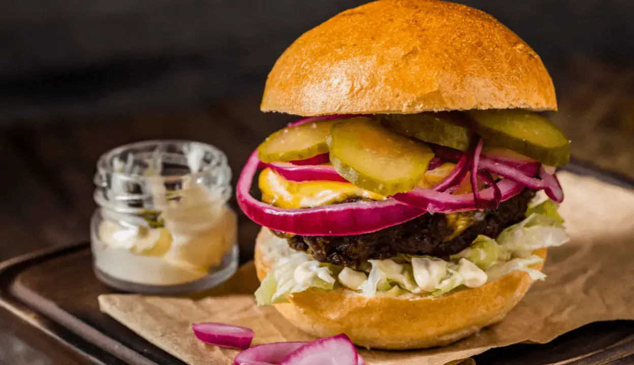 Soczysty burger z ogórkiem, czerwoną cebulą i majonezem, idealny do przygotowania, jak smażyć burgera na patelni.