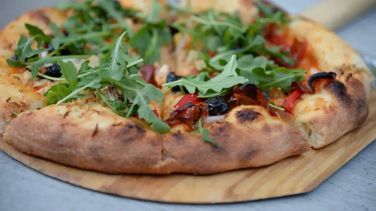 Idealne ciasto na pizzę z rukolą, oliwkami i papryką, wypieczone na drewnianej desce.