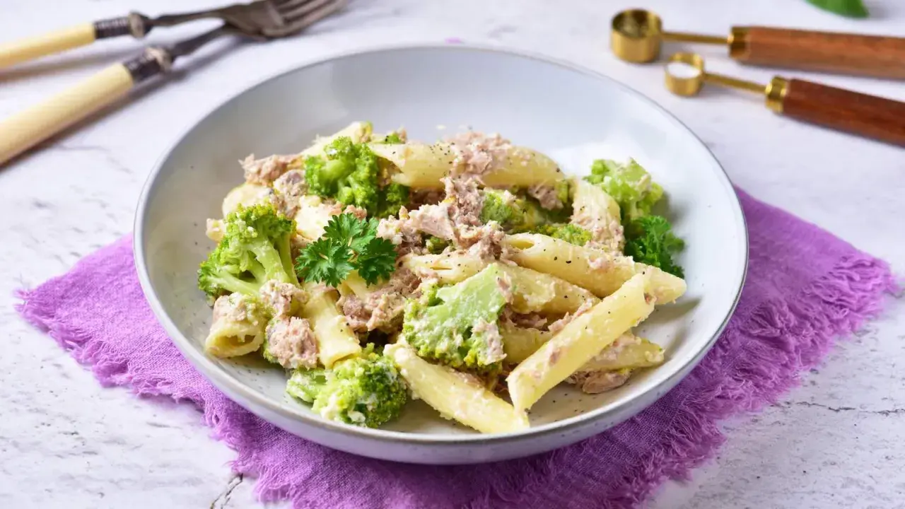 Penne z tuńczykiem i brokułami w kremowym sosie śmietanowo-serowym, udekorowane natką pietruszki.