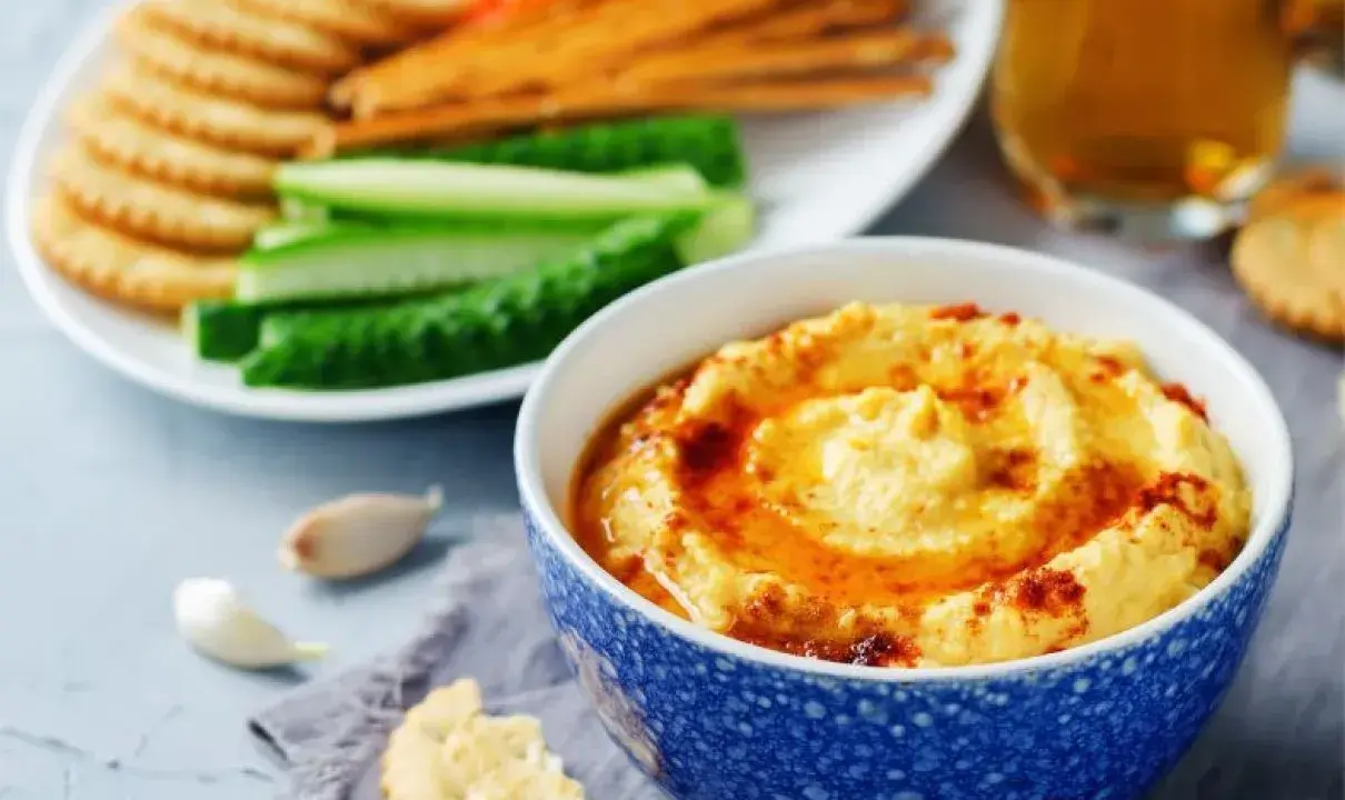 Pyszny, kremowy hummus, idealny jako sos do frytek, podany z chrupiącymi krakersami i świeżymi warzywami.