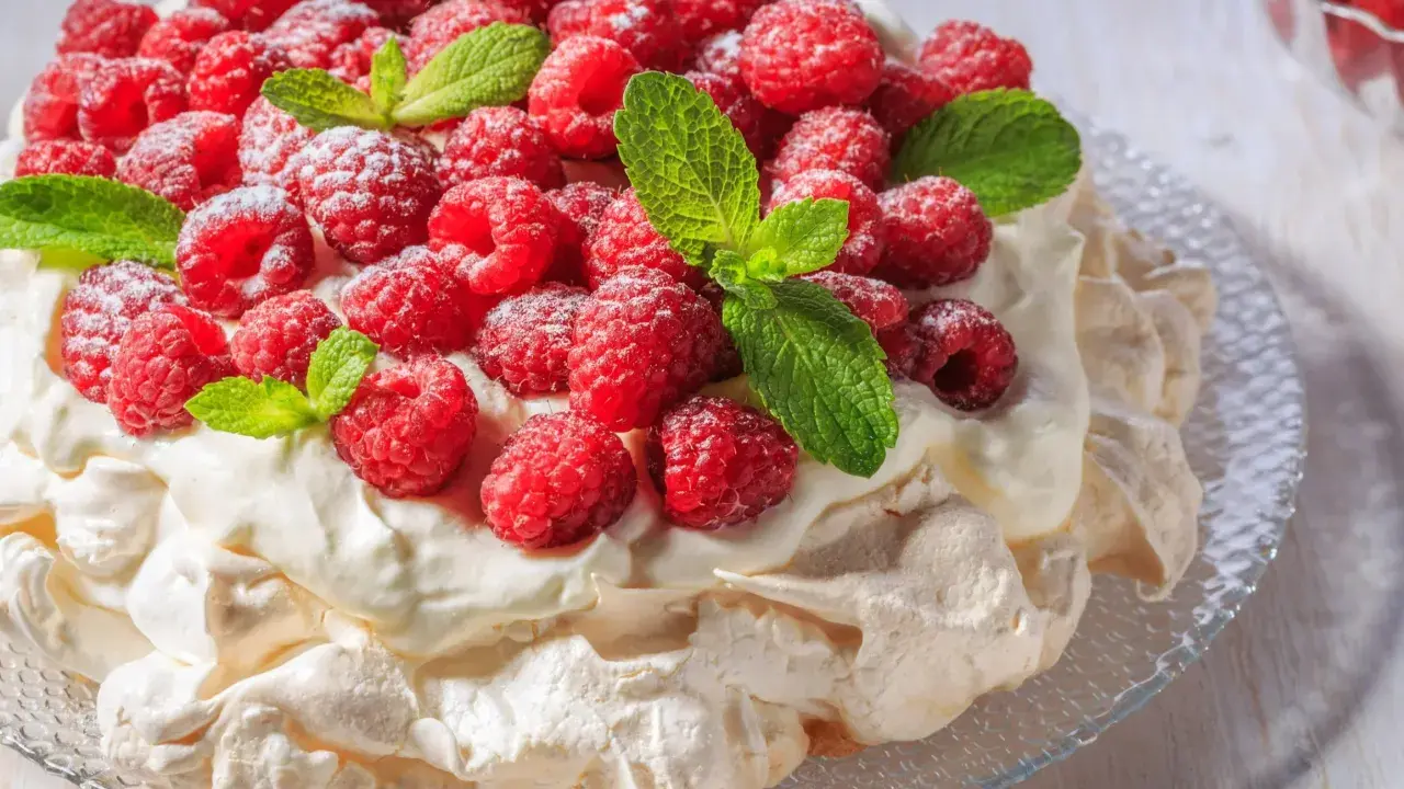 Beza Pavlova, która zawsze wychodzi, udekorowana świeżymi malinami i listkami mięty, posypana cukrem pudrem.