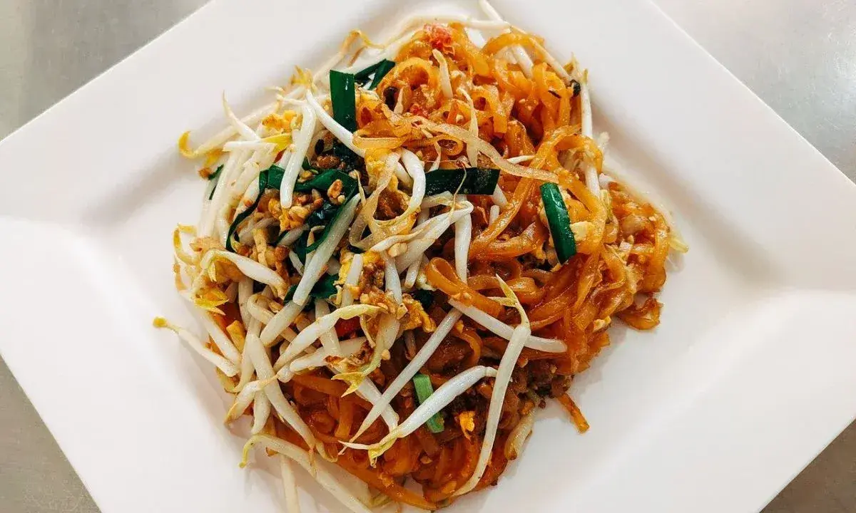 Pyszne pad thai co to? Danie z makaronem ryżowym, kiełkami fasoli mung, jajkiem i szczypiorkiem na białym talerzu.