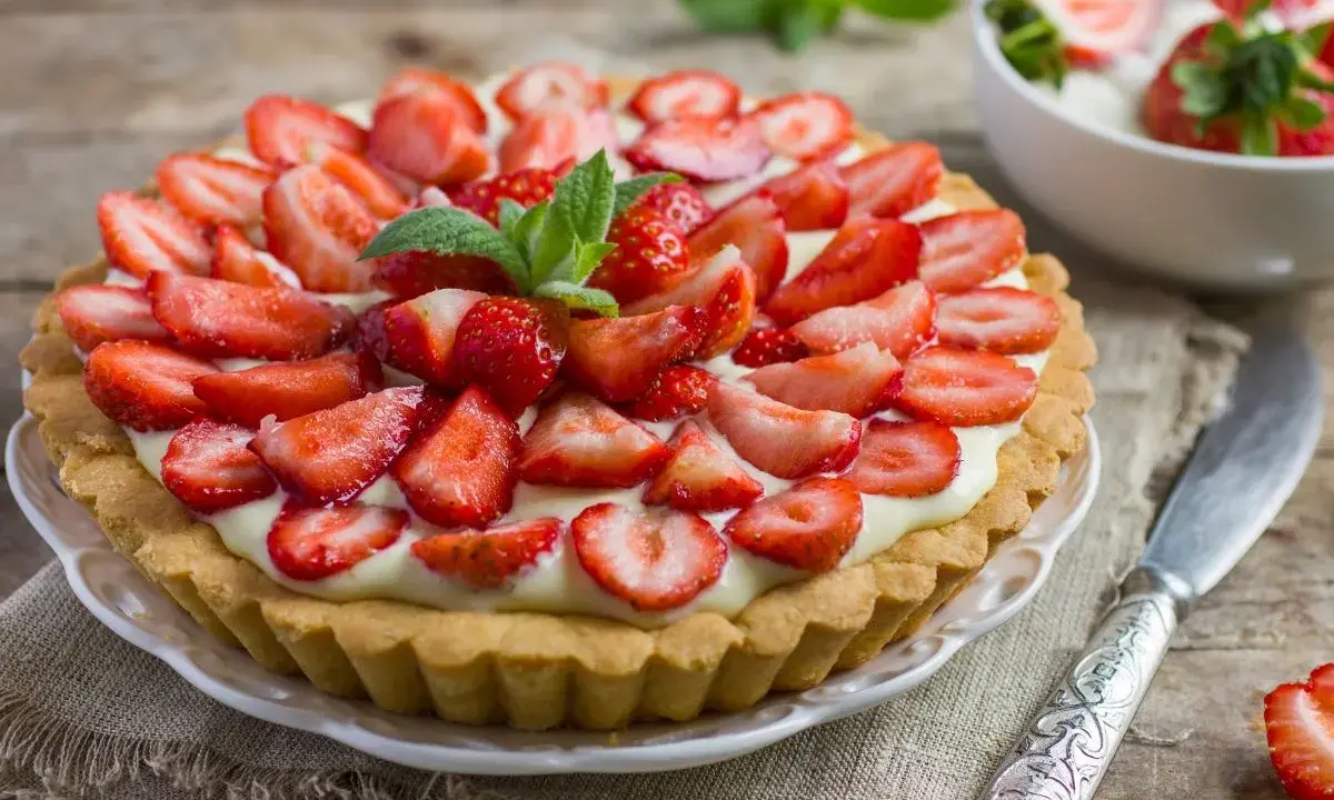 Pyszna tarta z truskawkami i kremem, ozdobiona listkami mięty. Idealna na letnie popołudnie.