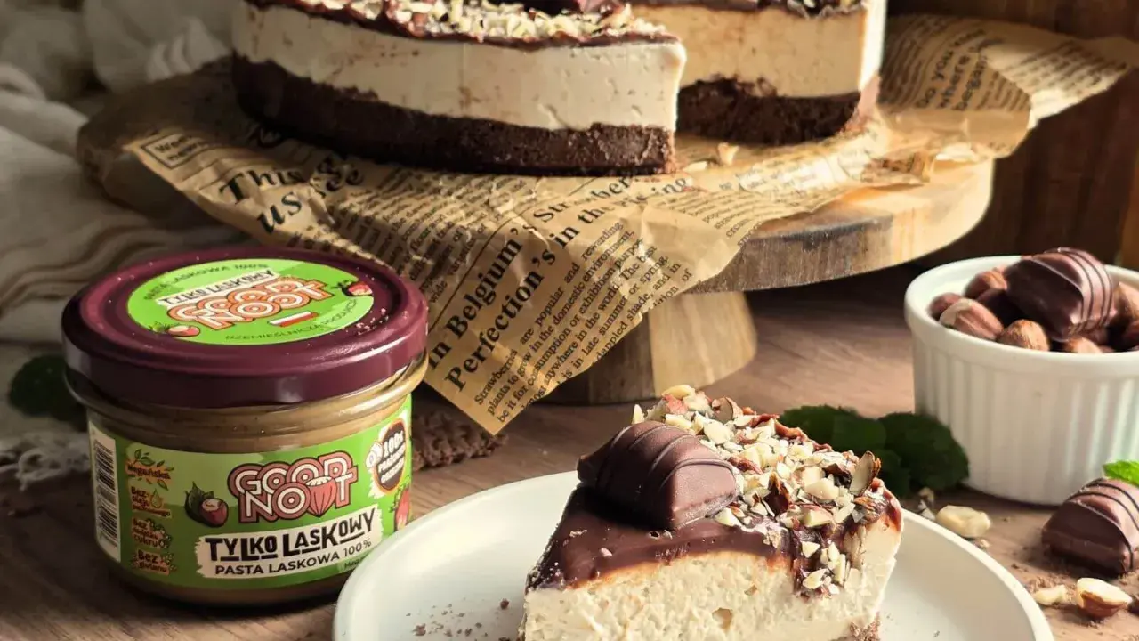 Pyszne ciasto kinder bueno z mascarpone, udekorowane orzechami i kawałkami czekolady. Obok słoik pasty z orzechów laskowych.