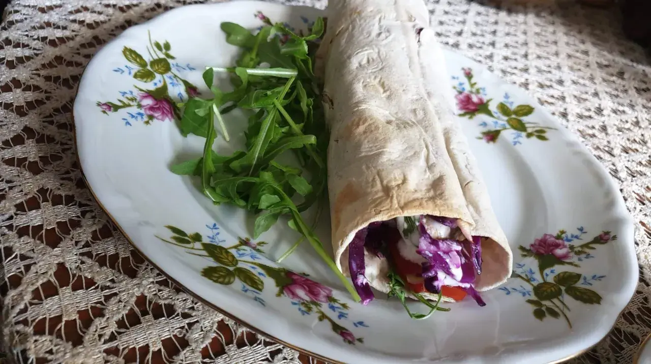 Pyszny lawasz kebab z czerwoną kapustą, pomidorem i rukolą na ozdobnym talerzu.