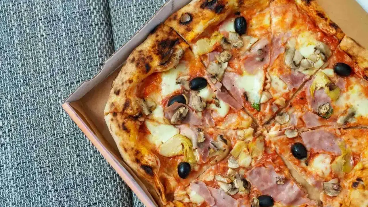 Pizza capricciosa z szynką, pieczarkami, karczochami i czarnymi oliwkami, w pudełku.