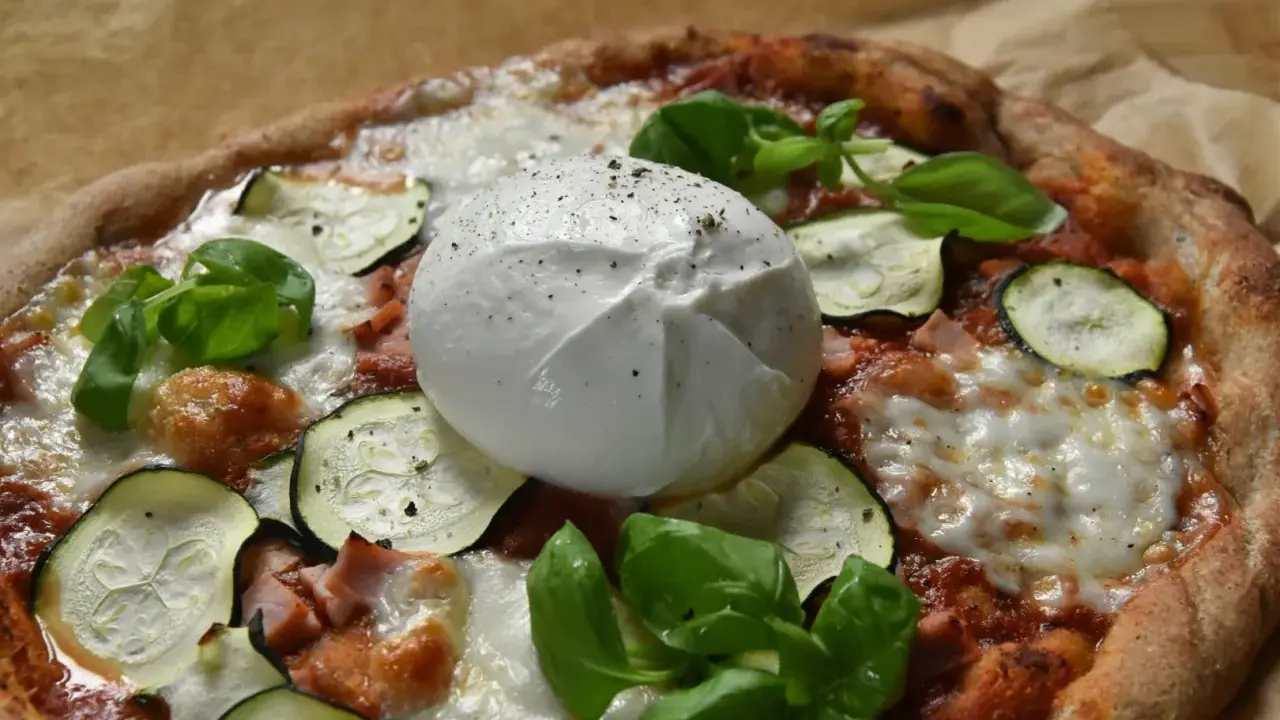 Pyszna pizza z burrata, cukinią i bazylią, posypana świeżo mielonym pieprzem.