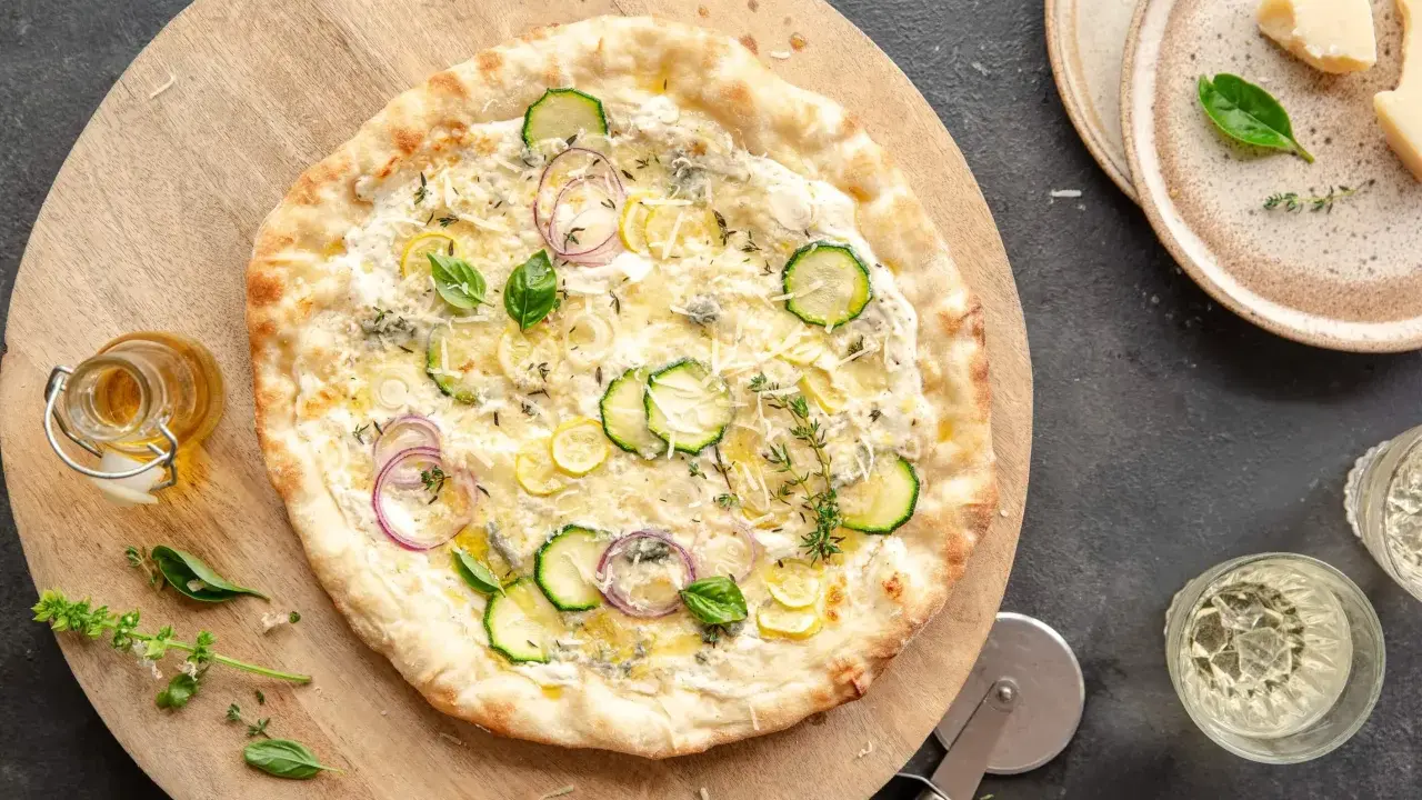 Pyszna pizza bianca z cukinią, cebulą i cytryną, posypana parmezanem i ziołami. Idealna na letni wieczór.