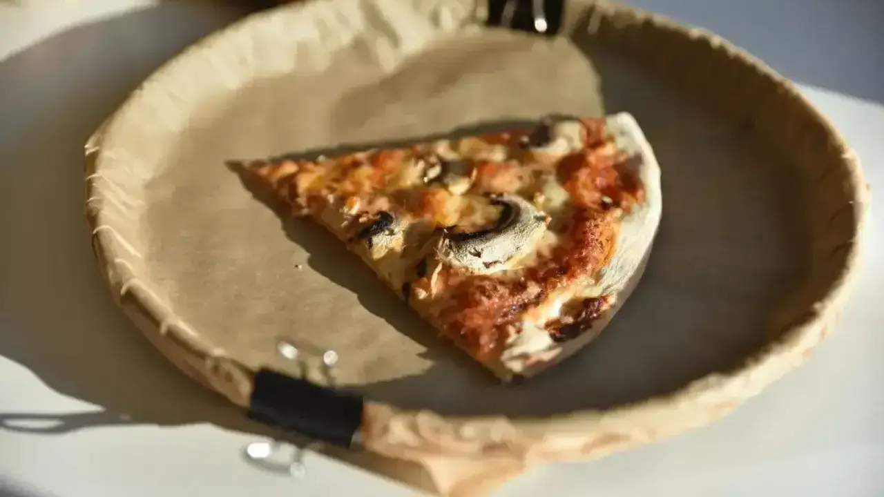 Kawałek pizzy z pieczarkami na papierowym talerzu. Zastanawiasz się, ile kalorii ma średnia pizza?