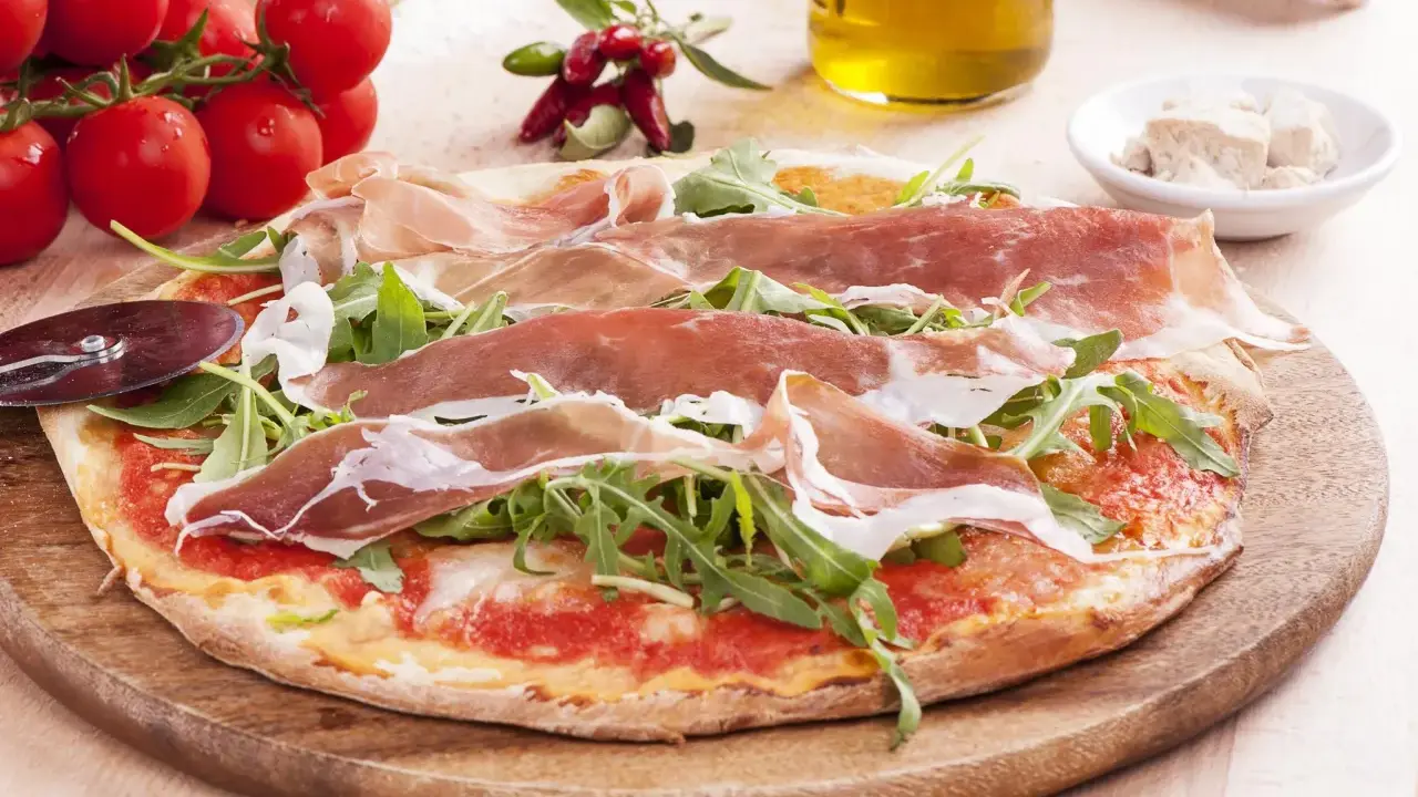 Pyszna pizza prosciutto z rukolą, pomidorami i oliwą z oliwek. Idealna na włoską ucztę.