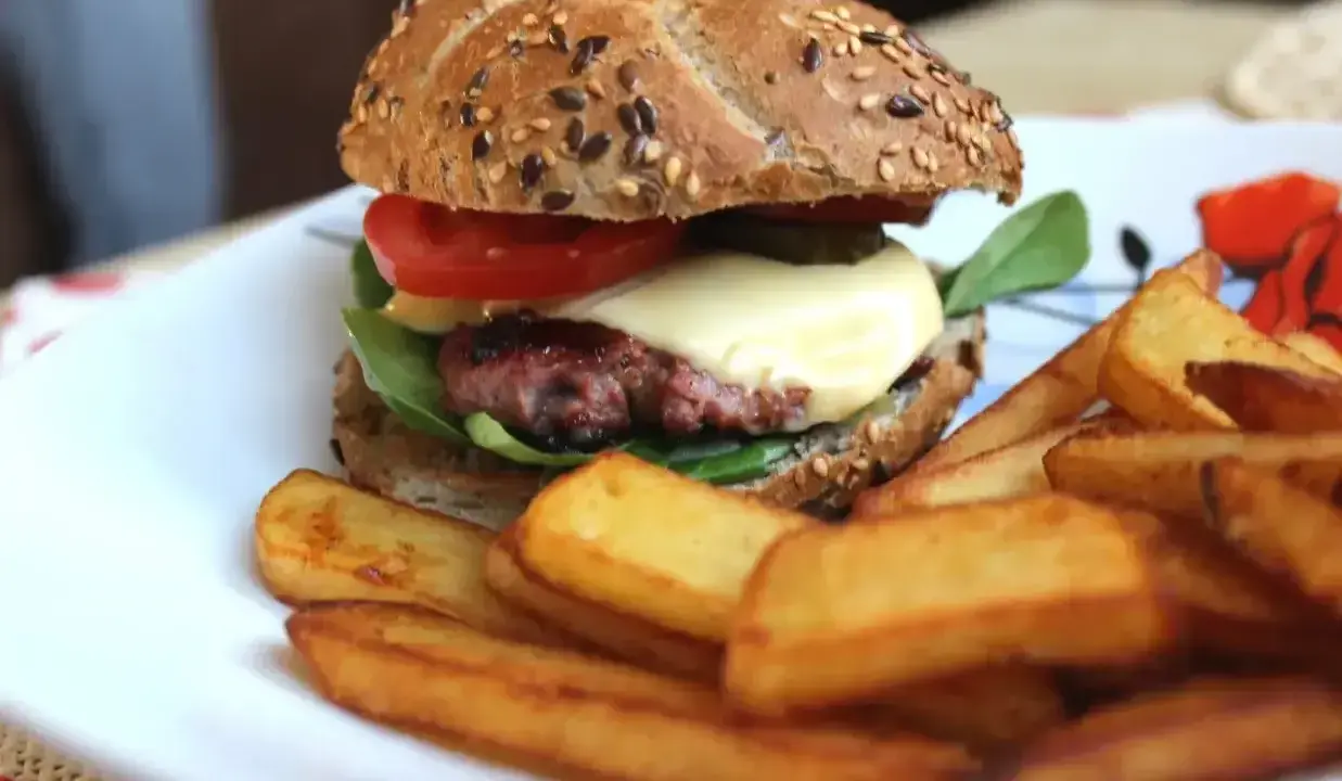 Pyszne, prawdziwe burgery przepis na domowy obiad. Soczysty kotlet, ser, warzywa i chrupiące frytki na talerzu.