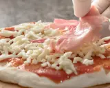 Rękawiczki zakładają cienkie plastry szynki parmeńskiej na pizzę z serem i sosem pomidorowym.