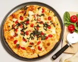 Pyszna pizza z serka wiejskiego, pomidorkami koktajlowymi i bazylią. Obok leży nóż do pizzy i świeże pomidory.