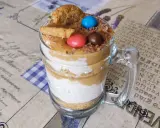 Warstwowy deser banoffee w szklance z polewą karmelową, bitą śmietaną, ciasteczkami i kolorowymi drażetkami.