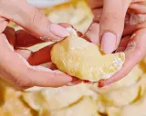 Dłonie z różowymi paznokciami lepią pierogi. Mąka lekko oprósza palce i ciasto. To idealny przepis na domowe pierogi.