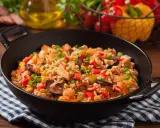 Pyszne jambalaya z kurczakiem, kiełbasą, kukurydzą i papryką w czarnej patelni.