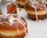 Lukier przepis na pączki. Łyżka polewa słodką masą pączki, które zaraz trafią na stół.