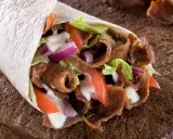 Pyszny, domowy kebab zawinięty w tortillę z soczystym mięsem, chrupiącą sałatą, pomidorami i cebulą, polany sosem.