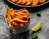 Chrupiące frytki z batatów z frytkownicy airfryer, podane w metalowym koszyku, z limonką i natką pietruszki.
