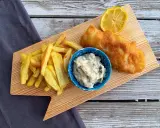 Chrupiące fish and chips z cytryną i sosem tatarskim na drewnianej desce.