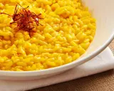 Aksamitne risotto alla milanese, złociste od szafranu, podane w białej misce, ozdobione nitkami szafranu.