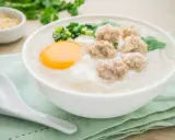 Miseczka aromatycznego congee z mięsnymi klopsikami, jajkiem i szczypiorkiem.