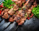Soczyste kawałki mięsa na szpadach, przypominające kofta kebab, podane z pieczoną papryką i świeżą natką pietruszki.