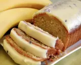 Puszyste ciasto bananowe na oleju, oblane kremowym lukrem, z kawałkami owoców. Obok leżą dojrzałe banany.